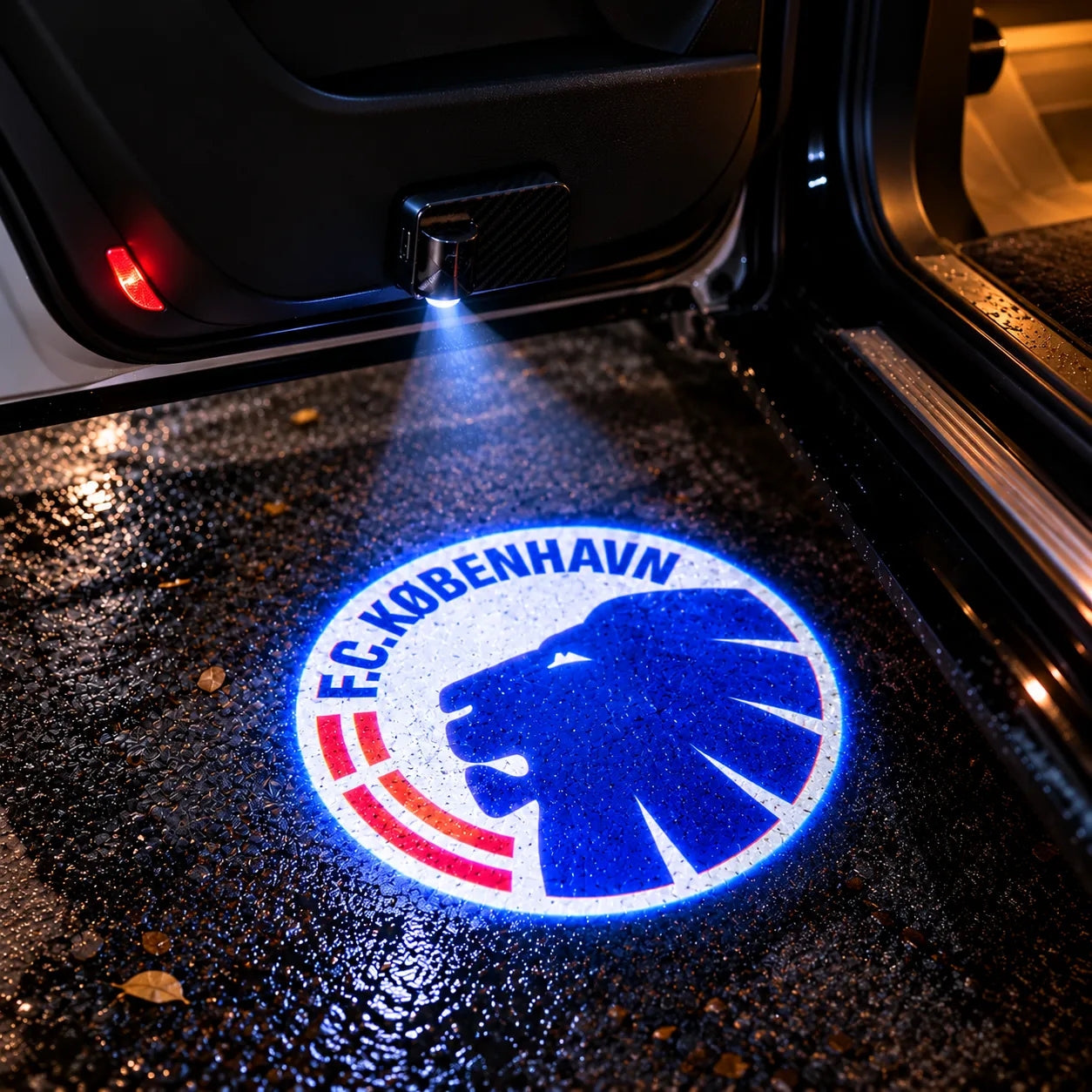 F.C. København-logo projiceret på våd asfalt under en åben bildør
